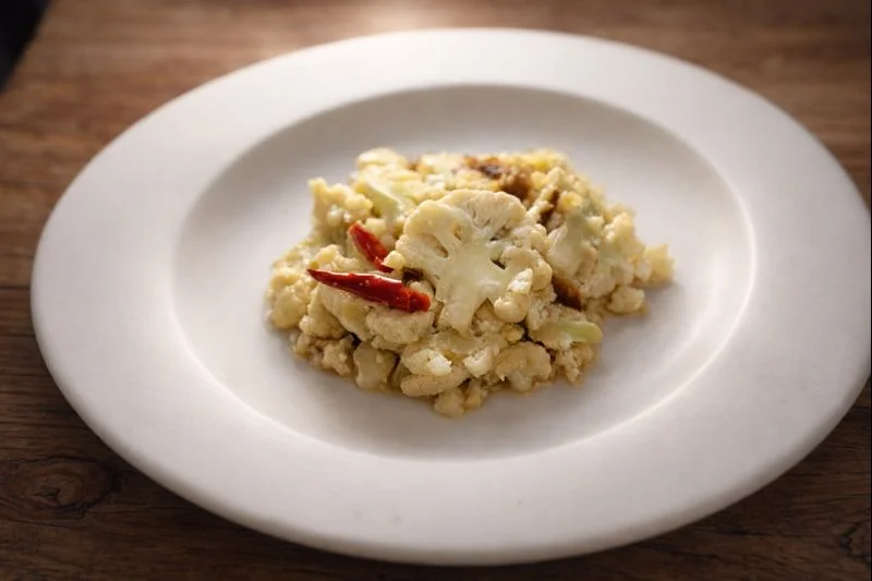 白い皿に盛りつけたカリフラワーのピクルス。やさしい色合いで、作り置きとして静かに食卓に並ぶ一皿