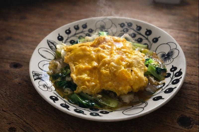 ターツァイとキャベツの炒め物の上に、半熟卵をふんわりのせた一皿。湯気が立ち、冬の食卓らしい温かさが伝わる