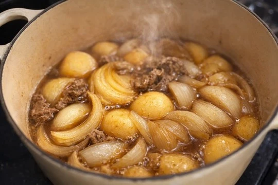 鍋の中で煮込まれる肉じゃが。玉ねぎと牛肉に煮汁が絡み、湯気が立ちのぼっている