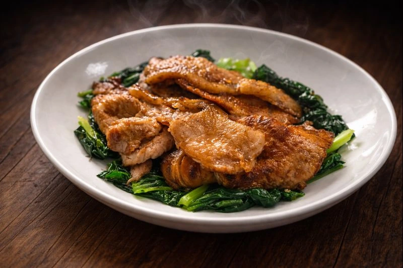 香ばしく焼いた豚のしょうが焼きを、艶のある青菜の上に盛り付けた一皿。湯気が立ち、冬の食卓が温まるような雰囲気