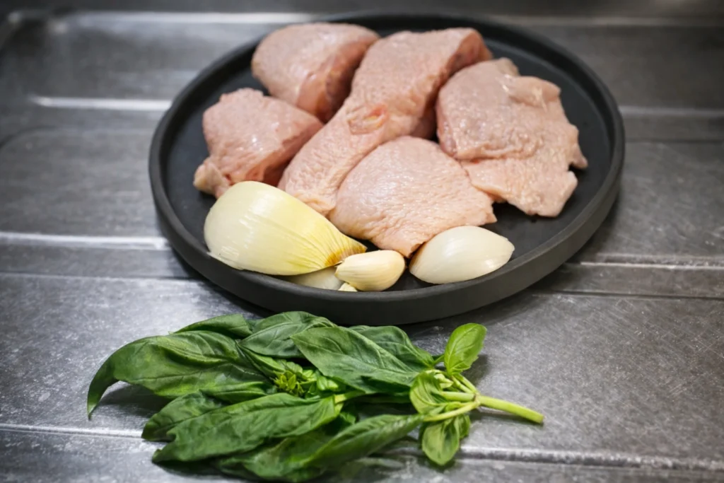 鶏肉、にんにく、玉ねぎ、バジルを並べたアドボの仕込み。静かな台所のステンレス台の上に整えられた材料