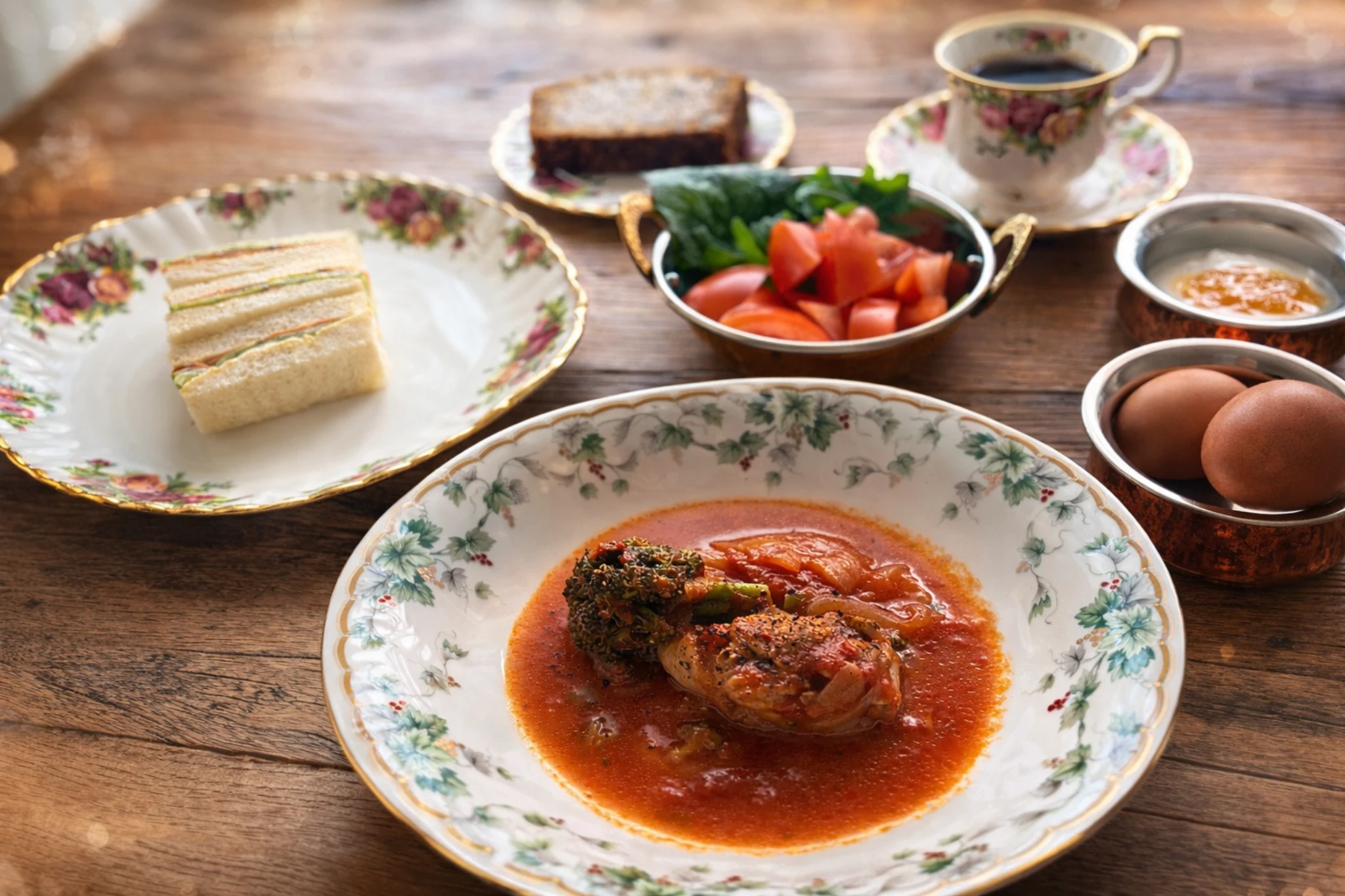 花柄のお皿に盛られたトマトスープと、サンドイッチや卵が並ぶ休日の朝ごはん。50代の丁寧な食卓。